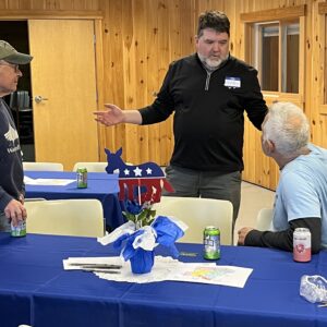 Senator Chip Curry speaks with Paul and Andre at a table decorated with a star-spangled red-white-and-blue centerpiece.