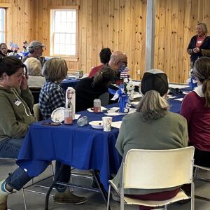 Rep. Jan Dodge addresses the spring potluck crowd seated at blue tablecloth covered tables